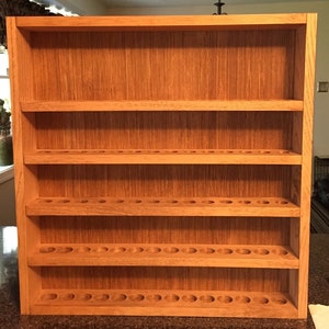 May include: A wooden shelf unit with five shelves, each with a row of evenly spaced circular holes. The shelf unit is made of light brown wood with a natural wood finish.