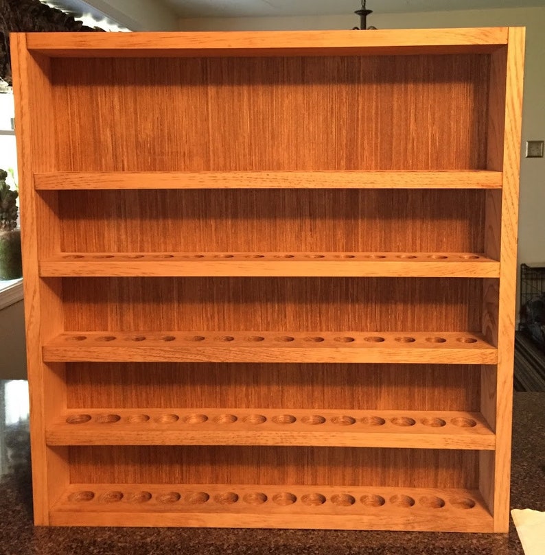 May include: A wooden shelf unit with five shelves, each with a row of evenly spaced circular holes. The shelf unit is made of light brown wood with a natural wood finish.