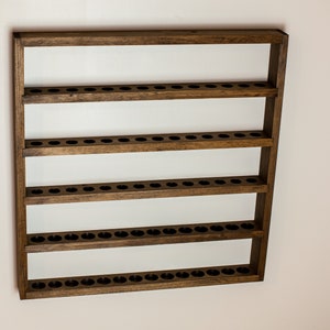 May include: A wooden wall-mounted shelf with five rows of evenly spaced holes, perfect for displaying small items like essential oils or nail polish.
