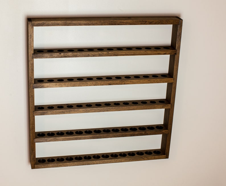 May include: A wooden wall-mounted shelf with five rows of evenly spaced holes, perfect for displaying small items like essential oils or nail polish.