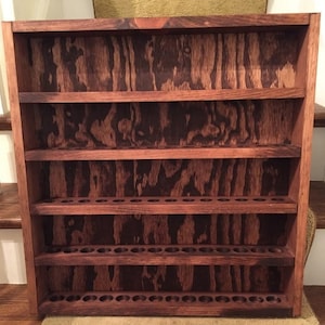 May include: A wooden shelf unit with five shelves and a dark brown stain. The shelves have a pattern of small holes on the front, likely for holding small bottles or tubes.