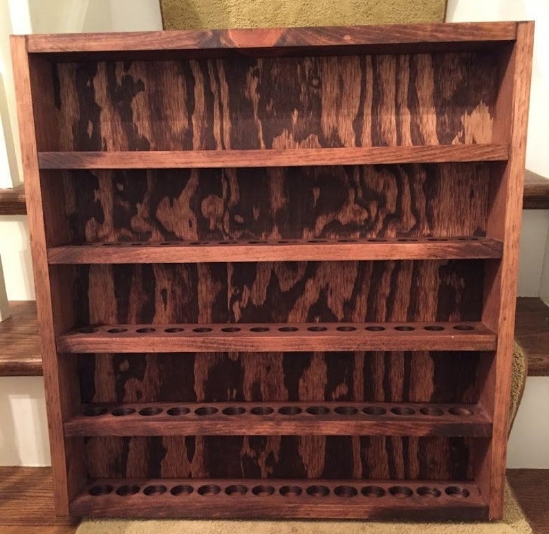 May include: A wooden shelf unit with five shelves and a dark brown stain. The shelves have a pattern of small holes on the front, likely for holding small bottles or tubes.