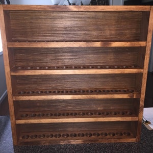 May include: A wooden shelf unit with five shelves, each with multiple circular holes. The shelves are stained a dark brown color.