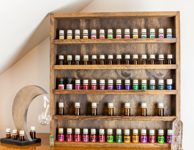 May include: Wooden shelf unit with five shelves, each holding rows of small glass bottles with white caps. The bottles are filled with colorful liquids. The shelf unit is made of dark brown wood with a rustic finish.