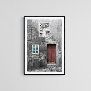 May include: A black and white photograph of a weathered building with a single blue window and a red wooden door. The building is in a state of disrepair, with cracks and peeling paint.