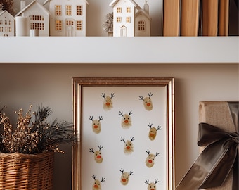 May include: A gold-framed print displaying reindeer faces with black antlers and red noses. The print is on a white shelf with decorative white houses, a woven basket, and a wrapped gift with a brown ribbon. Books are also on the shelf.