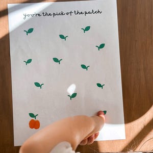 May include: A white rectangular paper featuring the black text you're the pick of the patch at the top. The paper is decorated with multiple small green leaf illustrations and one orange fingerprint pumpkin at the bottom left corner.