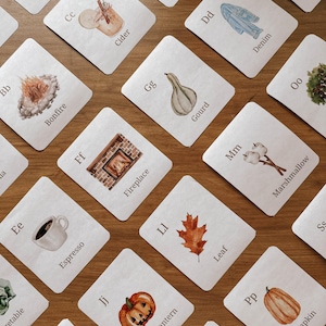 May include: A collection of illustrated flashcards with watercolor images and corresponding words. Cards feature images of a bonfire, cider, denim, espresso, fireplace, gourd, Jack O'Lantern, leaf, marshmallow, and pumpkin.