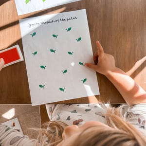 May include: White paper with green leaf stamps and the text "You're the pick of the patch". A red ink pad is visible. The image is taken from a child's perspective.