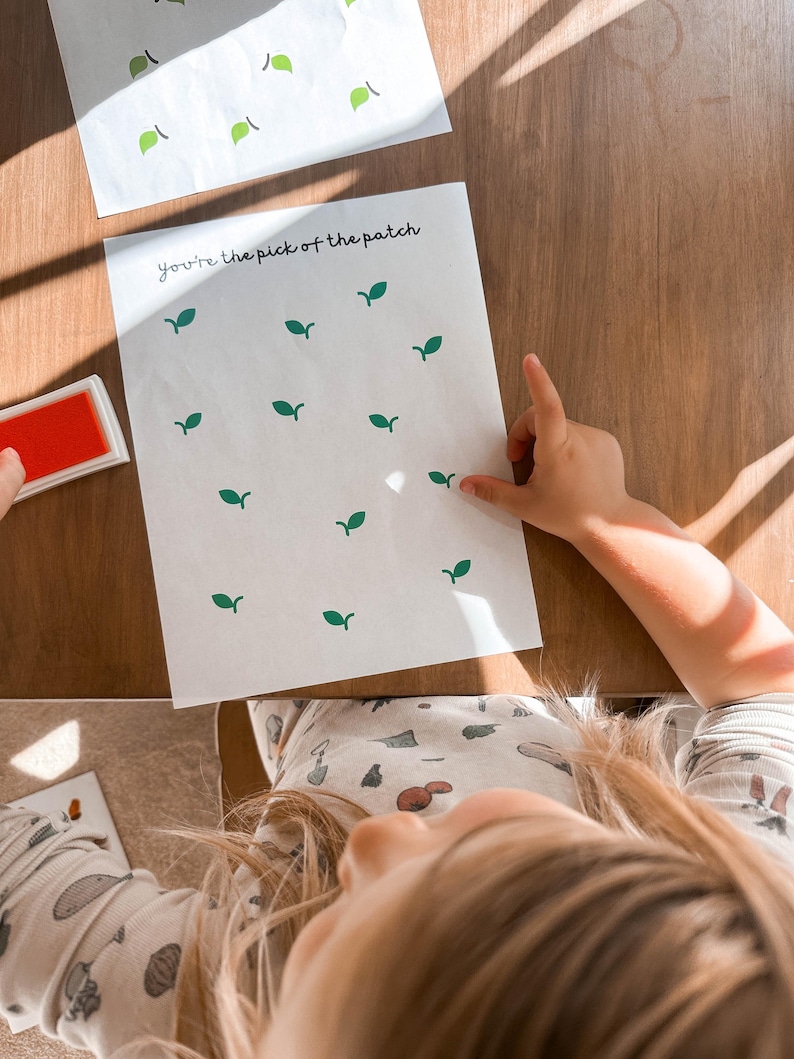 May include: White paper with green leaf stamps and the text "You're the pick of the patch". A red ink pad is visible. The image is taken from a child's perspective.