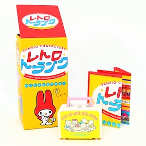 May include: A yellow box with the text "SANRIO CHARACTERS レトロ トランク" and a picture of Hello Kitty. The box is next to a smaller yellow box with the text "SANRIO CHARACTERS レトロ トランク" and a picture of Hello Kitty. There is also a small pink and yellow toy trunk with the text "NYA-NI-NYU-NYE-NYON" and a picture of Hello Kitty.