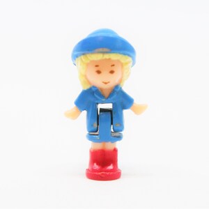 May include: A small plastic doll with blonde hair, wearing a blue dress, blue hat, and red shoes.