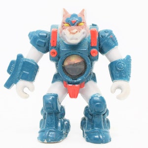 May include: A blue and white action figure of a wolf wearing a blue and red armoured suit. The figure has a red and yellow face and a clear plastic visor.