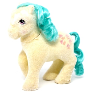 May include: A vintage My Little Pony toy with a cream-coloured body, turquoise blue mane and tail, and a pink and orange flower pattern on its flank.