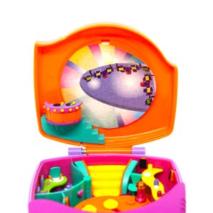 Puede incluir: Un juego de juguetes de pl&aacute;stico rosa y naranja con un escenario y una rueda giratoria. El escenario tiene un fondo morado con un dise&ntilde;o de arco&iacute;ris. La rueda giratoria tiene un dise&ntilde;o de arco&iacute;ris y un centro morado.