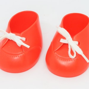 May include: A pair of bright orange baby shoes with white laces. The shoes have a simple design and are made of a smooth, shiny material.