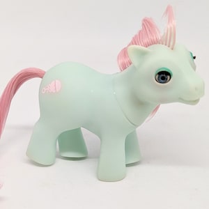 May include: A light blue My Little Pony with a pink mane and tail. The pony has blue eyes and a pink butterfly symbol on its side.