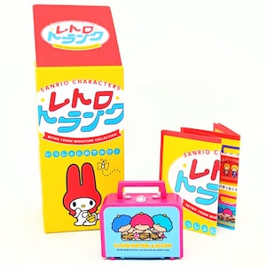 May include: A pink and blue miniature suitcase with a lock and wheels. The suitcase features a graphic of three cartoon characters with the text "GOROPIKADON" printed on the front. The suitcase is part of a Sanrio Characters Retro Trunk Miniature Collection.