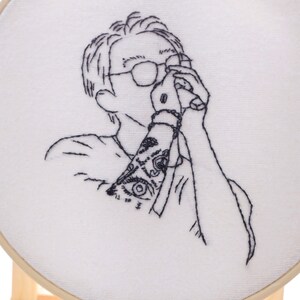 May include: Embroidered design of a person with a tattoo on their arm, holding a camera to their eye.