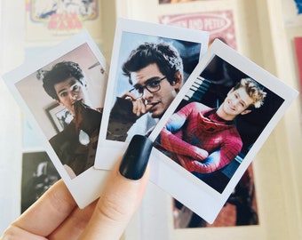 May include: Three Polaroid photos of a man in different poses. The first photo shows the man wearing a black shirt and looking at the camera. The second photo shows the man wearing a black shirt and glasses, looking at the camera. The third photo shows the man wearing a red and blue Spiderman costume, smiling at the camera.