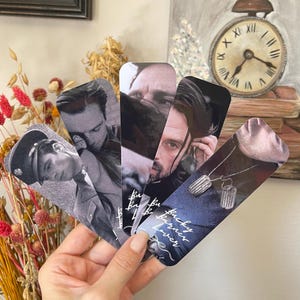 May include: A hand holds five bookmarks with black and white images of a man. The bookmarks are rounded at the top and rectangular. One bookmark has the text "Bucky Barnes Lover" in white script.