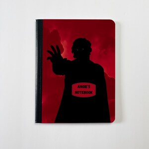 May include: A notebook with a black silhouette of a figure reaching out against a red background. The notebook has the text "ANGIE'S NOTEBOOK" on a red rectangle.