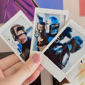 Op de afbeelding: Drie instant foto's, twee van een persoon met een blauwe en zilveren helm en een van een persoon met een bruine helm. De foto's zijn in witte frames met een witte rand.