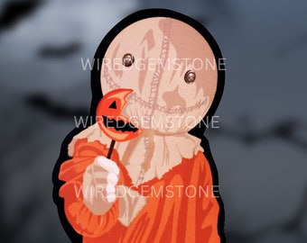May include: A sticker featuring a character with a burlap sack head, button eyes, and stitched mouth, wearing an orange hooded garment. The character holds a small orange pumpkin-shaped lollipop. The text WIREDGEMSTONE is overlaid on the image.