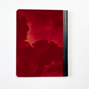 May include: A red notebook with a dramatic cloudscape design. The cover features a vibrant, deep red hue with darker cloud formations. The spine is a dark gray color, providing a contrast to the red cover. The notebook is set against a white background.