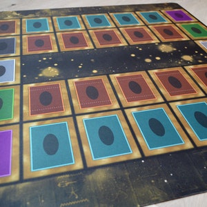 Puede incluir: Un tablero de juego con fondo negro y detalles dorados. El tablero tiene 25 casillas, cada una con un borde de color diferente y un c&iacute;rculo negro en el centro. Las casillas est&aacute;n dispuestas en una cuadr&iacute;cula de 5x5.
