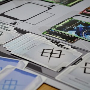 May include: A close-up of a tabletop game setup featuring various cards and a playmat. The cards have colorful illustrations and text, with a dominant color scheme of blue, green, and white. The playmat is gray with black outlines.