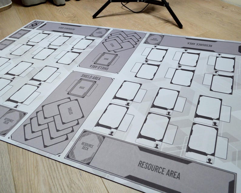 May include: A large, rectangular game mat with a gray and white design. The mat features labeled areas for resources, shields, and decks, with numerous card spaces. The overall design is geometric and organized, suitable for tabletop gaming.