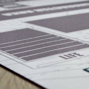 K&ouml;nnte beinhalten: Nahaufnahme einer gedruckten Grafik mit einem rasterartigen Design. Das Bild zeigt eine graue rechteckige Form mit horizontalen wei&szlig;en Linien, und das Wort "LIFE" ist sichtbar. Der Hintergrund ist hellgrau mit schwachen Linien.