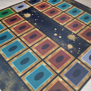 Puede incluir: Una estera de juego con fondo negro y detalles dorados. La estera tiene una cuadr&iacute;cula de 36 cuadrados, cada uno con un borde de color diferente. Los cuadrados est&aacute;n llenos de c&iacute;rculos negros. La estera est&aacute; dise&ntilde;ada para un juego de cartas.