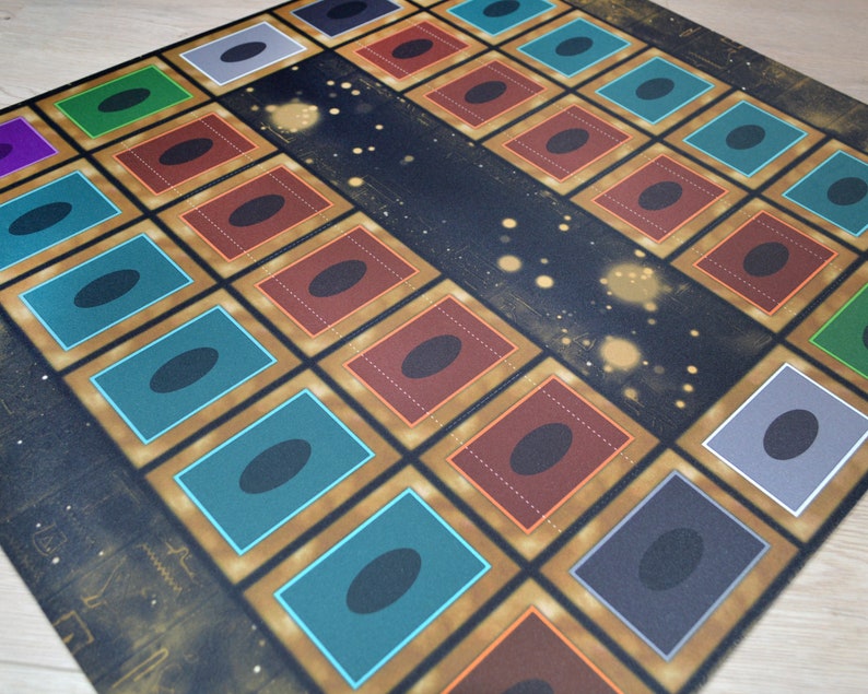 Puede incluir: Una estera de juego con fondo negro y detalles dorados. La estera tiene una cuadr&iacute;cula de 36 cuadrados, cada uno con un borde de color diferente. Los cuadrados est&aacute;n llenos de c&iacute;rculos negros. La estera est&aacute; dise&ntilde;ada para un juego de cartas.