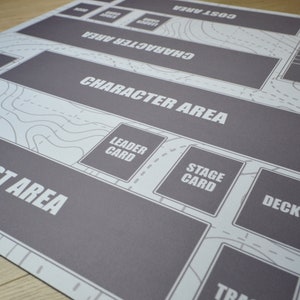 K&ouml;nnte beinhalten: Eine grau-wei&szlig;e Spielmatte mit beschrifteten Bereichen f&uuml;r das Gameplay. Die Matte enth&auml;lt Text wie "Character Area", "Cost Area" und "Deck". Das Design umfasst ein karten&auml;hnliches Muster mit Konturlinien und gestrichelten Linien.