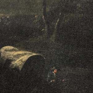 May include: A close-up of a dark denim fabric with a faded image of a landscape scene. The image appears to be of a forest with a large tree in the background and a small figure in the foreground.