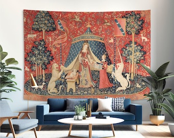 May include: A large tapestry with a medieval scene, featuring a woman, a unicorn, and a lion. The tapestry has a red background with blue and green accents, and is hanging above a blue sofa in a living room.
