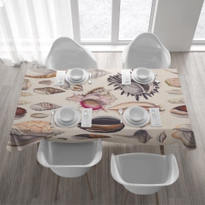Può includere: Una tovaglia beige con un motivo a conchiglie. La tovaglia è apparecchiata con quattro coperti, ognuno con una ciotola bianca, due forchette e un coltello. La tovaglia è su un tavolo di legno con quattro sedie bianche.