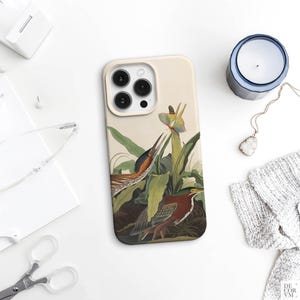 May include: A beige phone case featuring a detailed illustration of two birds amidst lush green foliage and a yellow flower. The artwork has a vintage, botanical print style. The case is on a white surface with other accessories.