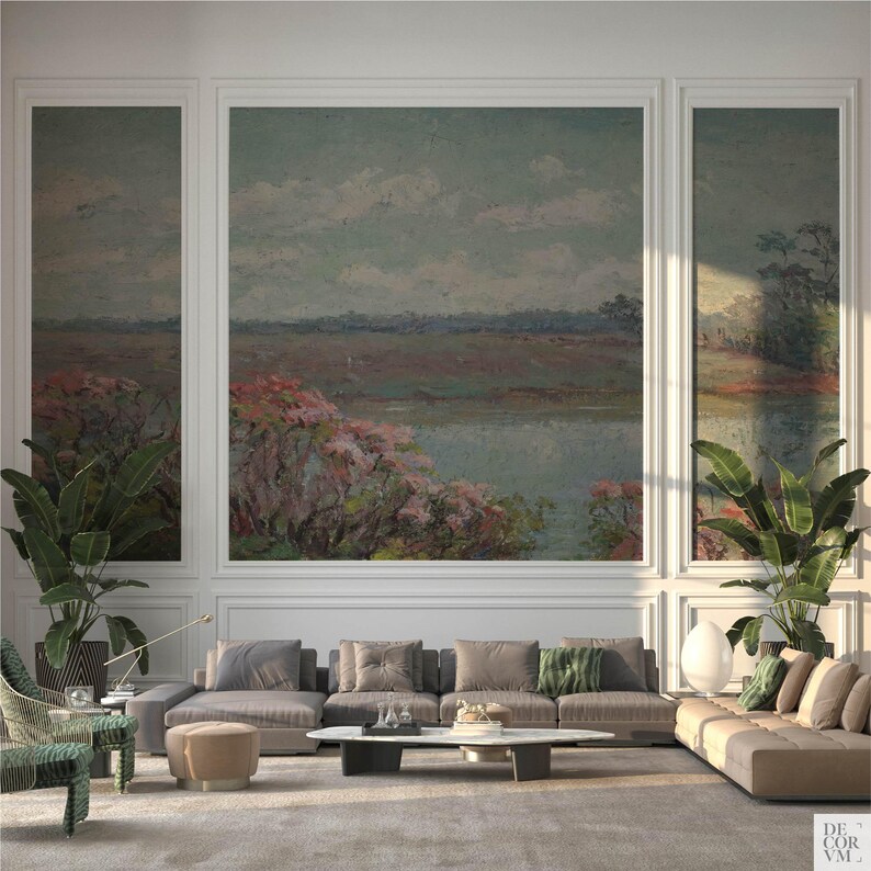 May include: A living room with a large landscape painting above a sectional sofa. The painting depicts a body of water with pink and green foliage. The room features large potted plants, a coffee table, and a patterned armchair.