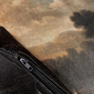 May include: Close-up of a black zipper on a pillowcase with a brown and green landscape print.