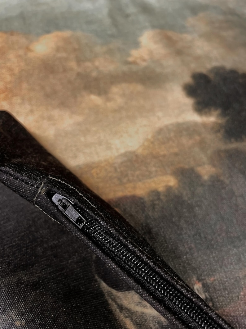 May include: Close-up of a black zipper on a pillowcase with a brown and green landscape print.