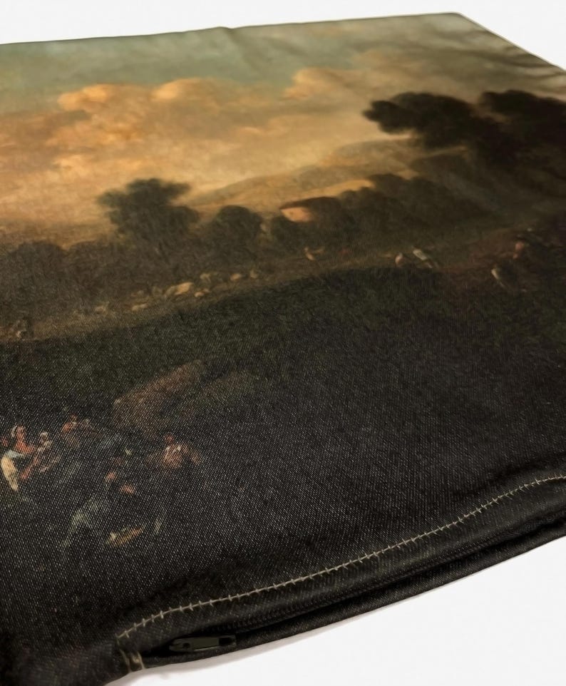 May include: A black pillow with a zipper closure. The front of the pillow features a printed image of a landscape painting with a cloudy sky and a group of people in the foreground.