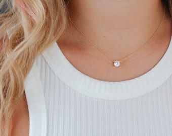 May include: A delicate gold chain necklace with a single, round, clear gemstone pendant.