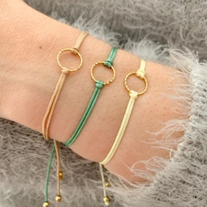 May include: Three bracelets with gold circle charms. The bracelets are made of thin string in beige, light green, and cream.