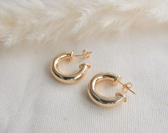 May include: A pair of gold hoop earrings. The earrings are thick and have a smooth, polished finish.