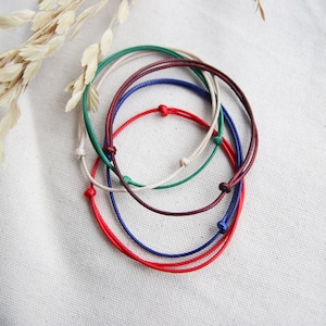 May include: Five colorful string bracelets in red, blue, green, white, and maroon. The bracelets are tied together in a knot.