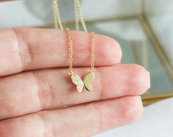 Pode incluir: Um colar de corrente de ouro com um pequeno pingente de borboleta. A borboleta é incrustada com pequenas pedras transparentes.