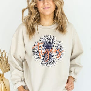 May include: A beige sweatshirt with a navy blue and orange graphic of a baseball with the word "Tigers" written in orange.